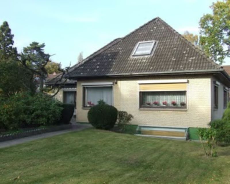 Einfamilienhaus mit weißer Fassade und schwarzem Dach, davor eine grüne Rasenfläche